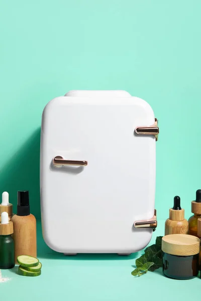 Small refrigerator with natural cosmetics and ingredients on green background