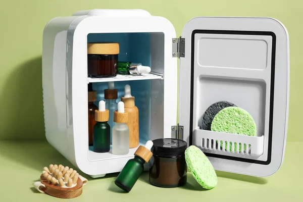 Small refrigerator with natural cosmetics, sponges and massage brush on green background