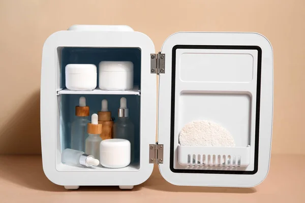 Small refrigerator with natural cosmetics and sponge on beige background