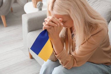 Ukrayna bayrağıyla evde dua eden olgun bir kadın.