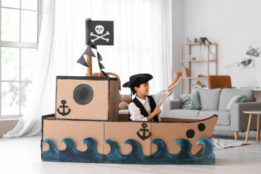 Korsan gibi giyinmiş küçük çocuk evde karton gemide iple oynuyor.