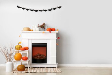 Ağaç dalları, merdiven, Cadılar Bayramı balkabakları ve ışık duvarı yakınında şömine olan vazolar.