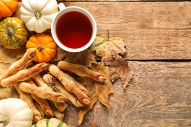 Bir fincan çay, balkabağı ve ahşap arka planda düşmüş yapraklı cadı parmak kurabiyeleri.