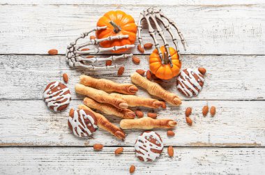 Cadılar Bayramı kurabiyeleri, balkabağı, iskelet eller ve beyaz ahşap arka planda badem fıstığı.