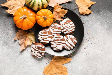 Cadılar Bayramı mumya kurabiyeleri, balkabakları, siyah beyaz arka planda düşmüş yapraklar.