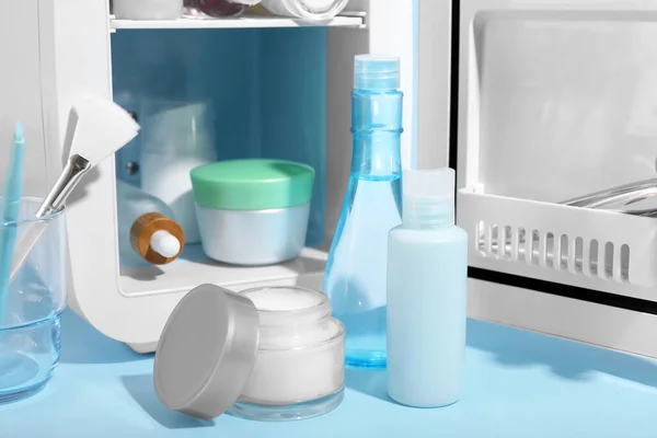 Small refrigerator with cosmetics on blue background, closeup