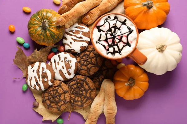 Halloween cookies with fallen leaves, pumpkins, candies and drink on violet background