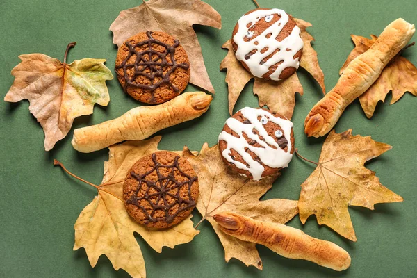 Tasty Halloween cookies with fallen leaves on green background