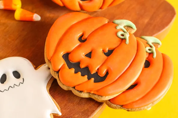 Sarı arka planda lezzetli Cadılar Bayramı kurabiyeleri olan tahta, yakın plan.