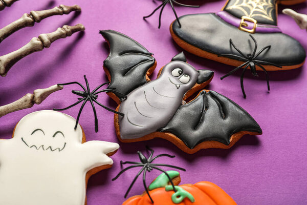 Tasty Halloween cookies and skeleton hand on purple background, closeup