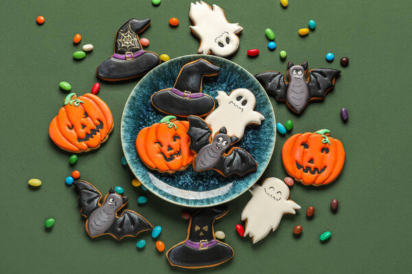 Bowl with Halloween cookies and candies on green background