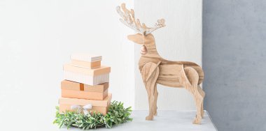 İçinde Noel çelengi, hediye kutuları ve ışık duvarının yanındaki tahta ren geyiği olan masa.