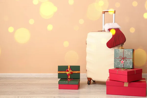 Suitcase with Santa Claus sock and gift boxes near wall. Christmas vacation concept