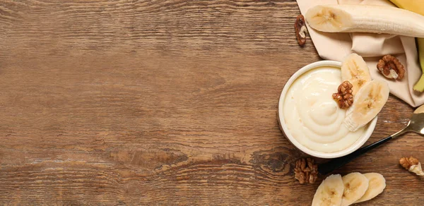 Bowl of delicious vanilla pudding and banana on wooden background with space for text