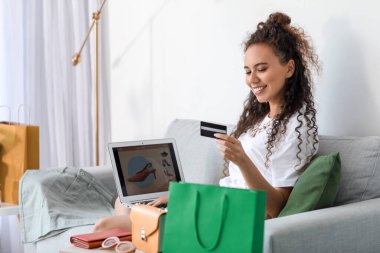 Kredi kartı ve dizüstü bilgisayarı olan genç bir Afro-Amerikalı kadın evde online alışveriş yapıyor.