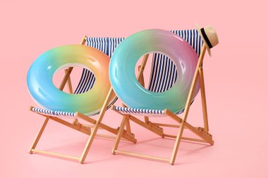 Plaj sandalyeleri ve pembe arka planda şişme halkalar.