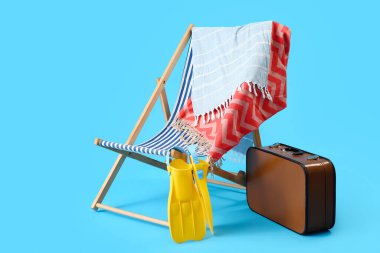 Güverte koltuğu, bavul ve açık mavi arka planda plaj aksesuarları.