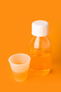 Bir şişe öksürük şurubu ve turuncu arka planda bir fincan.