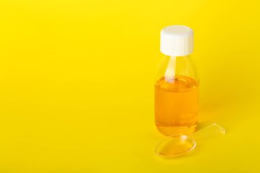 Sarı arka planda şişe ve kaşık öksürük şurubu.