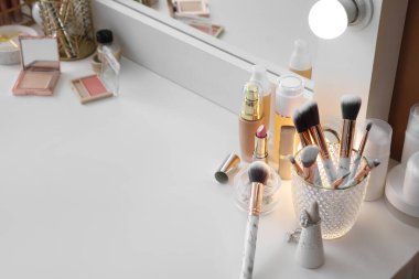Bej duvarın yanındaki masada makyaj fırçaları ve dekoratif kozmetik ürünleri olan tutucu.