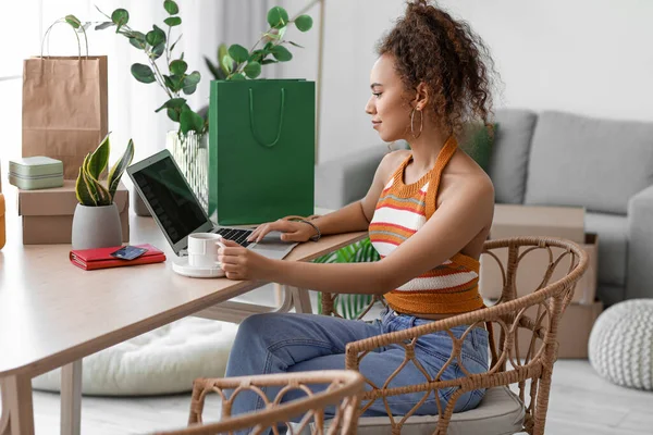 Bir fincan kahve ve dizüstü bilgisayarı olan genç bir Afro-Amerikalı kadın internetten alışveriş yapıyor.