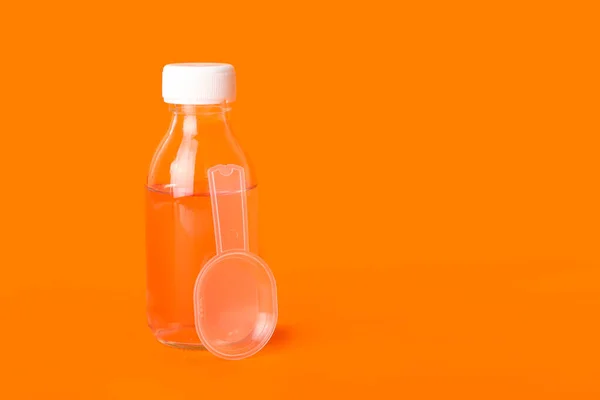 Bottle of cough syrup and spoon on orange background