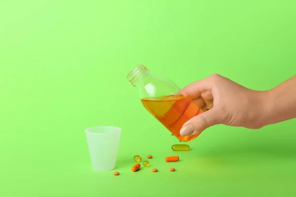 Woman with bottle of cough syrup, cup and pills on green background