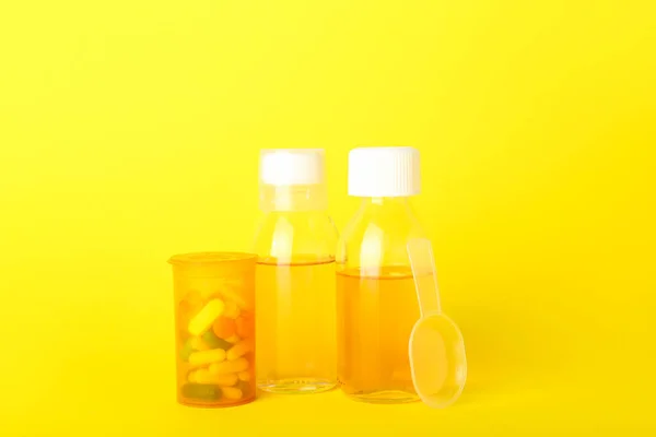 Bottles of cough syrup, pills and spoon on yellow background