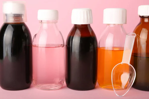 Bottles of cough syrup and spoon on pink background