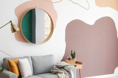 Oturma odasındaki renkli duvarda asılı duran zarif yuvarlak ayna.