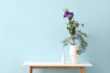 Mavi duvarın yanındaki masada güzel ikebana vazoları var.