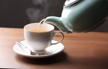 Kafedeki masaya demlikten fincana sıcak çay dökülüyor.