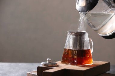 Elektrikli çaydanlıktan, gri arka plandaki çay demliğine sıcak su dökülüyor.