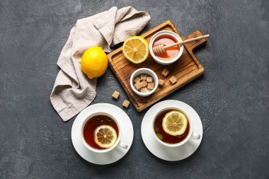 Koyu arkaplanda siyah çay, limon, yemek, kamış şekeri ve bal kaseleri.