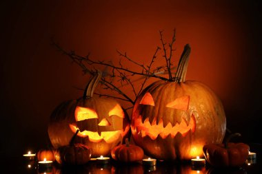 Cadılar Bayramı balkabakları, yanan mumlar ve arka planda ağaç dalları.