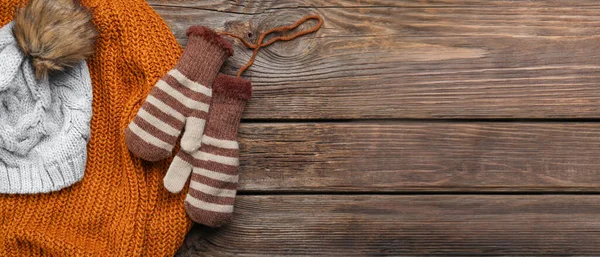Warm mittens with knitted sweater and hat on wooden background with space for text