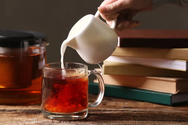 Woman pouring milk from jug into glass cup at table