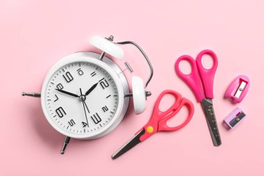 Renk arkaplanında alarm saati, makas ve bileyiciler