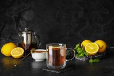 Koyu arkaplanda limon, nane ve bal olan bir bardak siyah çay.