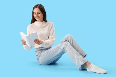 Güzel bir kadın mavi arka planda kitap okuyor.