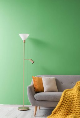 Yastıklı gri kanepe, ekose ve lamba yeşil duvarın yanında.