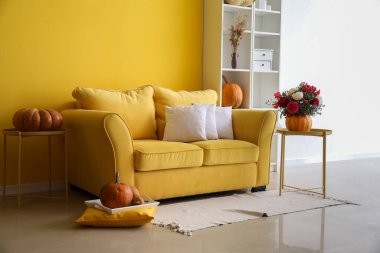 Kanepe, balkabağı ve çiçeklerle dolu parlak sarı oturma odasının içi.