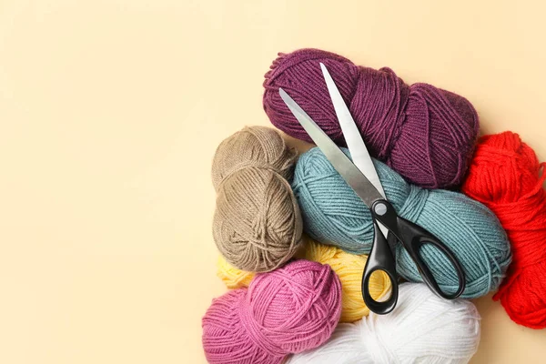 Scissors and knitting yarn on color background