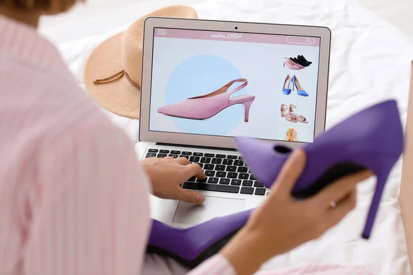 Young woman with new shoes using laptop in bedroom, closeup. Online shopping