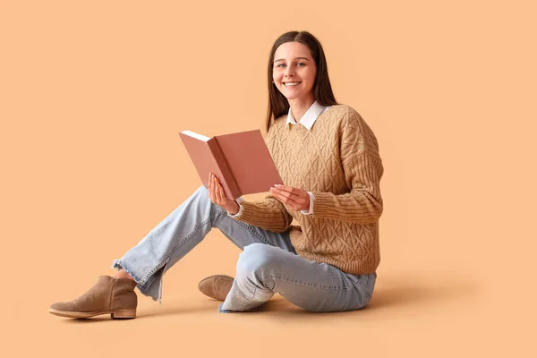 Beautiful woman with book sitting on beige background