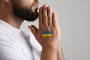 Ukrayna bayrağını çekmiş genç adam gri arka planda dua ediyor, yakın plan