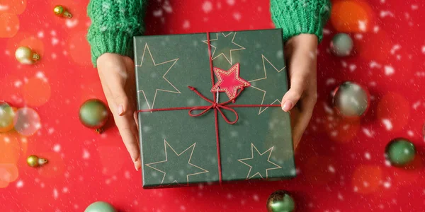 Frauenhände Mit Geschenkschachtel Und Weihnachtskugeln Auf Rotem Hintergrund Ansicht Von — Stockfoto