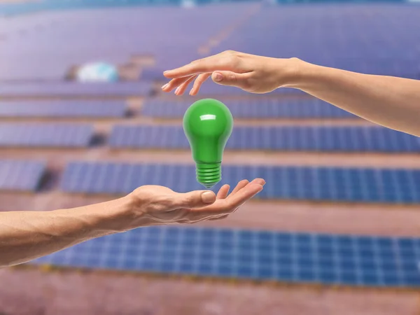 Hands with green light bulb against blurred solar power plant