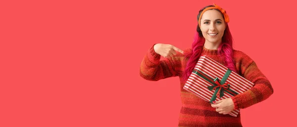 Güzel Bir Kadın Kırmızı Arka Planda Noel Hediyesine Işaret Ediyor — Stok fotoğraf