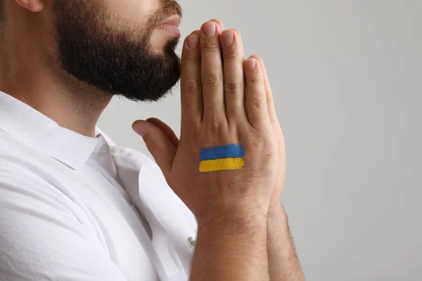 Young man with drawn flag of Ukraine praying on grey background, closeup